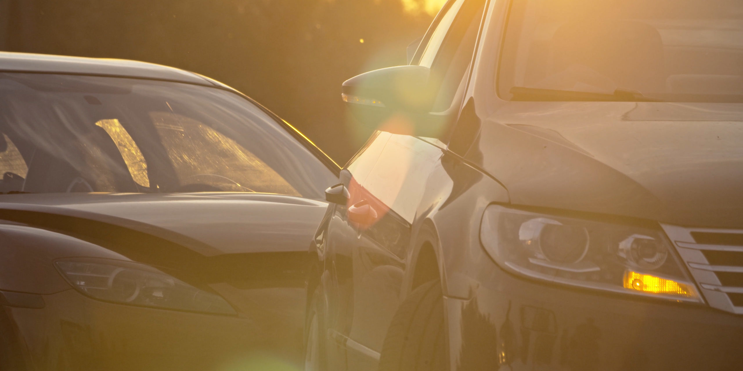Car accident in the city. View of two modern cars crashed standing stuck on the road at sunset. Traffic collision.